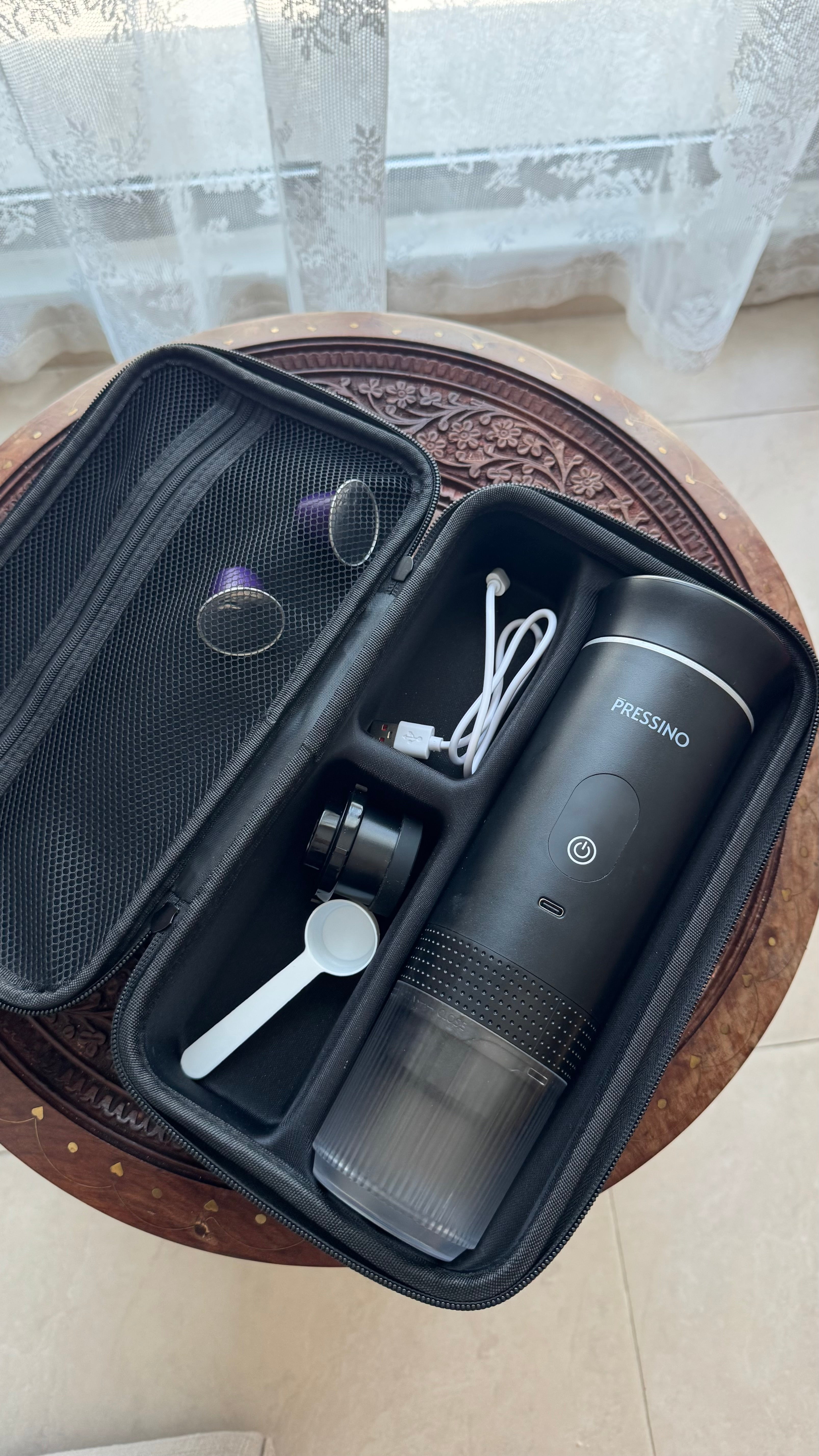 Open Pressino One travel case revealing the portable espresso maker neatly secured inside, placed on a carved wooden surface under soft daylight, highlighting premium craftsmanship, organization, and travel-ready design.