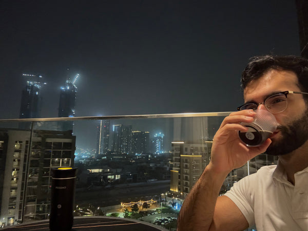 Man drinking from a cup with a cityscape view at night